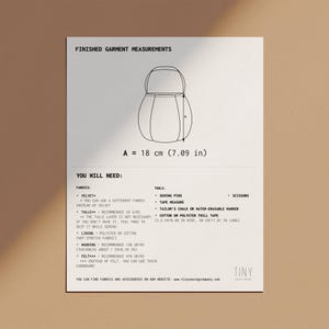 Op de afbeelding: Een zwart-wit diagram dat de afmetingen van een afgewerkt kledingstuk laat zien. Het diagram toont een afgeronde vorm met een aanduiding "A = 18 cm (7,09 inch)". De tekst "U heeft nodig:" wordt vermeld met een lijst van stoffen en gereedschappen die nodig zijn om het kledingstuk te maken. De tekst "U kunt stoffen en accessoires vinden op onze website: www.tinysewingcompany.com" staat onderaan het diagram.