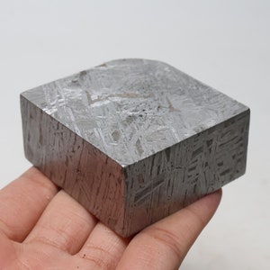 May include: A rectangular piece of meteorite with a silvery-gray color and a textured surface. The meteorite has a Widmanstätten pattern, which is a characteristic pattern of iron-nickel crystals.