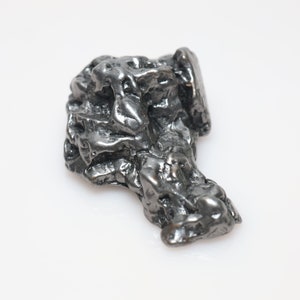 May include: A dark grey, metallic meteorite with a rough, irregular surface. The meteorite has a unique, organic shape.