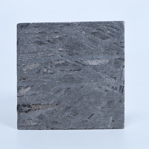 May include: A square-shaped iron meteorite fragment featuring a distinct Widmanstätten pattern of intersecting metallic bands. The surface displays a dark gray, weathered texture with visible crystalline structures and a small rust-colored spot.