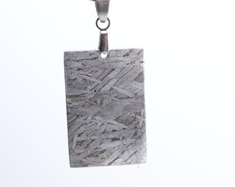 May include: A silver chain necklace with a rectangular pendant made of a meteorite. The pendant has a unique pattern of lines and swirls.