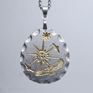 Könnte beinhalten: Silberfarbener Anhänger mit goldenem Sonnenstrahl-Design, Vögeln und einem Stern. Der Anhänger hängt an einer silbernen Kette. Der Anhänger hat eine strukturierte Oberfläche. Ca. 4 cm lang.