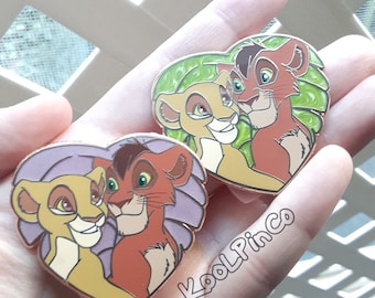 May include: Two heart-shaped enamel pins featuring a pair of lion cubs. One pin has a green leaf background, and the other has a purple background. Both pins depict the same two cubs with tan and reddish-brown fur. The text KoolPinCo is visible.