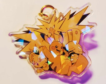 May include: A clear, iridescent acrylic charm featuring several cartoon characters in shades of yellow and orange. The charm has a gold-colored ring at the top for attachment. The characters are arranged in a group, with a spiky, lightning-like figure in the background.
