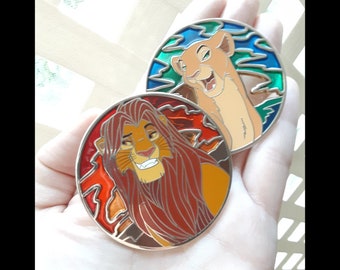 May include: Two round, metal pins featuring stained glass designs of Simba and Nala from the Disney movie The Lion King. The Simba pin has a red, orange, and yellow background with a brown lion with a red mane. The Nala pin has a blue, green, and yellow background with a tan lioness with a brown mane.