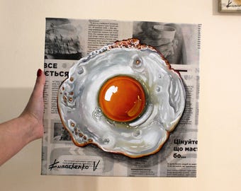 May include: A painting of a fried egg on a newspaper background. The egg yolk is a bright orange and the white is a creamy white. The newspaper text is in Cyrillic.