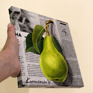 May include: A square canvas print featuring a realistic painting of a bright green pear with two dark green leaves attached to its stem. The pear is superimposed over a black and white background of printed newspaper text and a small photograph.
