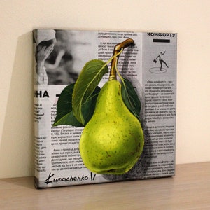 May include: A square canvas painting featuring a realistic green pear with a brown stem and two dark green leaves. The pear is layered over a background of black and white printed newspaper text in Ukrainian, with the signature Kumachenko V. at the bottom.