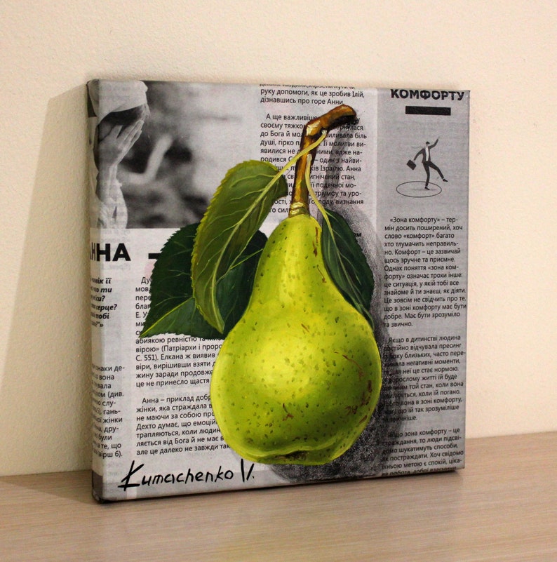 May include: A square canvas painting featuring a realistic green pear with a brown stem and two dark green leaves. The pear is layered over a background of black and white printed newspaper text in Ukrainian, with the signature Kumachenko V. at the bottom.