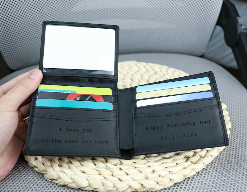 May include: A black leather wallet with a mirror on the inside. The wallet has a card slot and is engraved with the text 'I love you to the moon and back' on one side and 'Happy Birthday Dad 12.11.2021' on the other side.