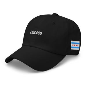 May include: Black baseball cap with white embroidered text reading "CHICAGO". The cap displays the Chicago city flag on the side. A fashionable accessory for fans of the city.