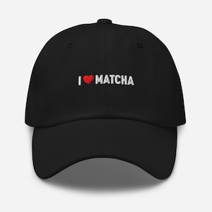 Puede incluir: Gorra de béisbol negra con el texto "I ♥ Matcha" bordado en blanco. El símbolo del corazón es rojo. La gorra tiene una visera curva y una correa ajustable en la parte trasera.