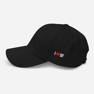 May include: Black baseball cap with a curved brim. The cap features the embroidered text "I ❤️ SF" in white and red thread on the side. The cap is made of a soft material and has an adjustable strap.