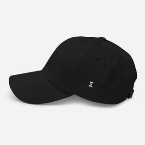 Puede incluir: Gorra de béisbol negra con visera curva y una pequeña letra griega sigma blanca bordada en el lateral. La gorra tiene un diseño clásico de seis paneles y una correa ajustable en la parte trasera.