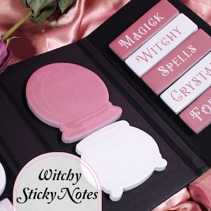 May include: A set of pink and white sticky notes with a witchy theme. The notes feature words like "Magick", "Witchy", "Spells", "Crystals", and "Fortune". There are also illustrations of a crystal ball and a cauldron.