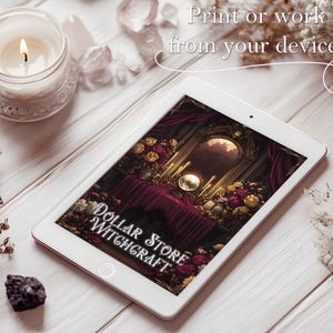May include: A white tablet displays an image with the text "Dollar Store Witchcraft." The image features a table with candles, flowers, and a mirror. A lit candle in a glass jar and crystals are also visible.