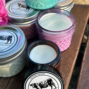 May include: A close-up of a jar of tallow sunscreen with a black and white label that says "Pasture Grazed Tallow Sunscreen Est. 2023 Memphis, MO". The jar is sitting on a wooden surface.