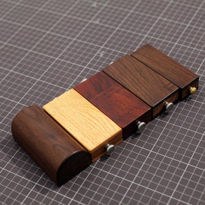 May include: Five wooden blocks of different colors and wood grains, stacked on top of each other. The blocks are connected with metal screws. The blocks are on a gray grid background.