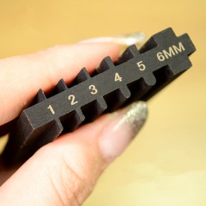 May include: A black plastic gauge with numbers 1 through 6 and the text "6MM" printed on it.