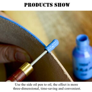 May include: A close-up of a person using a side oil pen to apply oil to a piece of leather. The oil pen has a blue tip and a wooden handle. A small bottle of blue oil is in the background.