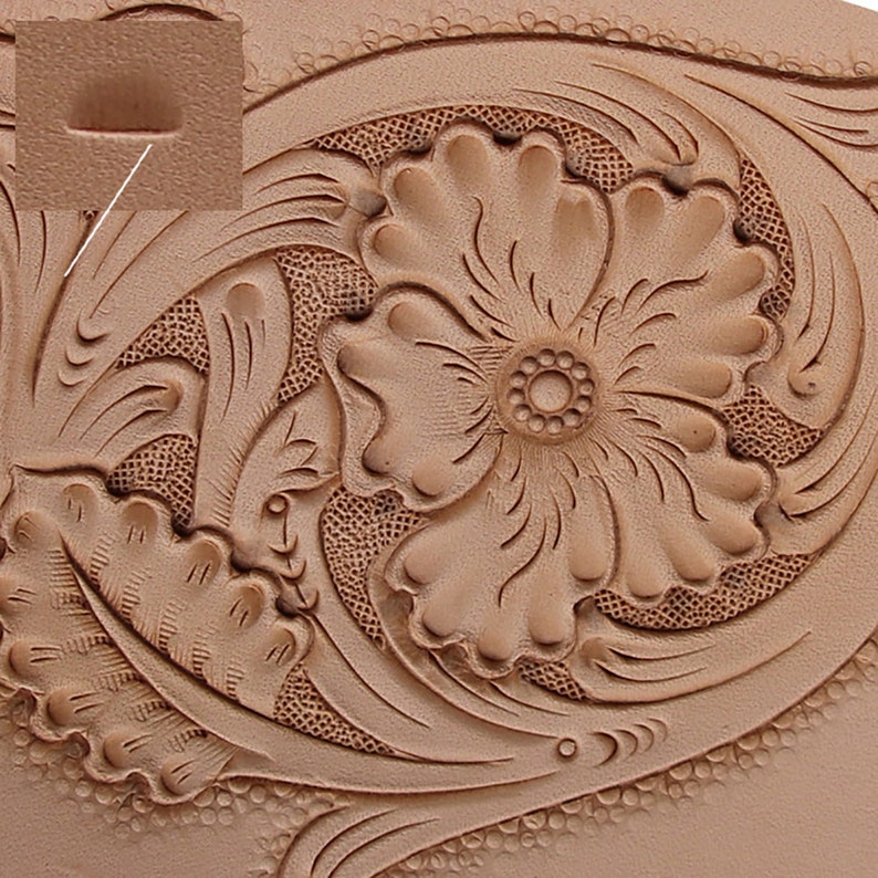 May include: Close-up of a tan leather surface with intricate floral and leaf tooling. The design features a large, detailed flower at the center, surrounded by swirling leaves and decorative patterns. The leather has a natural, textured appearance.