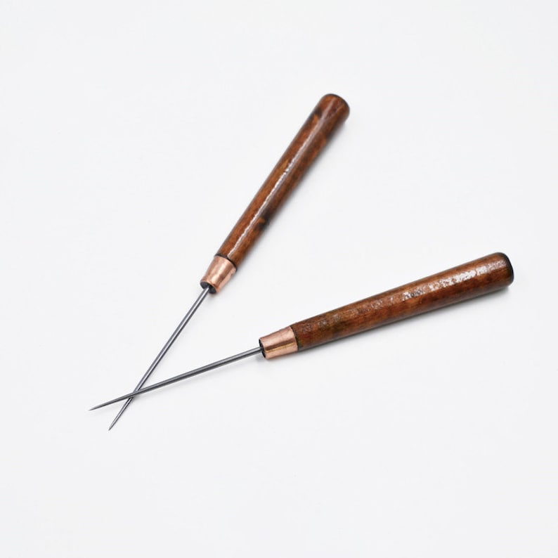 May include: Two wooden-handled awls with metal tips. The awls are crossed over each other.