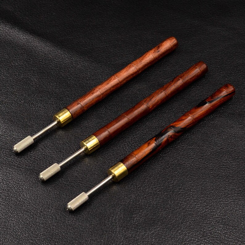 May include: Three wooden tools with metal tips. The tools have a brown and black wood grain pattern. The tools are laid out on a black surface.