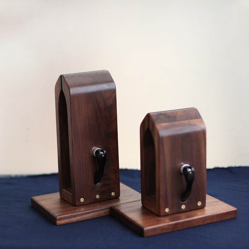 Puede incluir: Dos soportes de guitarra de madera con una perilla negra en cada uno. Los soportes son de madera oscura y tienen una base cuadrada.