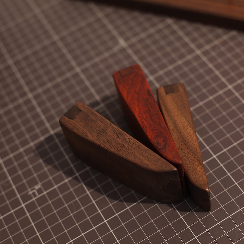 May include: Three wooden wedges, one red, one brown, and one dark brown, with metal accents. The wedges are arranged in a triangular shape on a gray grid surface.