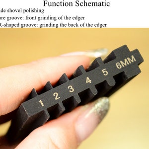 May include: A black tool with six grooves, each labeled with a number from 1 to 6. The last groove is labeled "6MM".