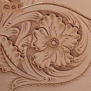 Op de afbeelding: Close-up van een lederen handwerkproject met een bloemmotief. Het ontwerp heeft een grote bloem met een kleinere bloem in het midden. Het leer is lichtbruin van kleur en heeft een getextureerd oppervlak.