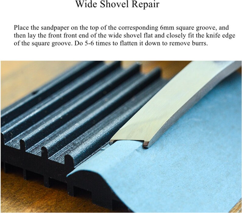 May include: A close-up of a blue sanding block being used to smooth the edge of a metal shovel. The shovel is resting on a black grooved surface.
