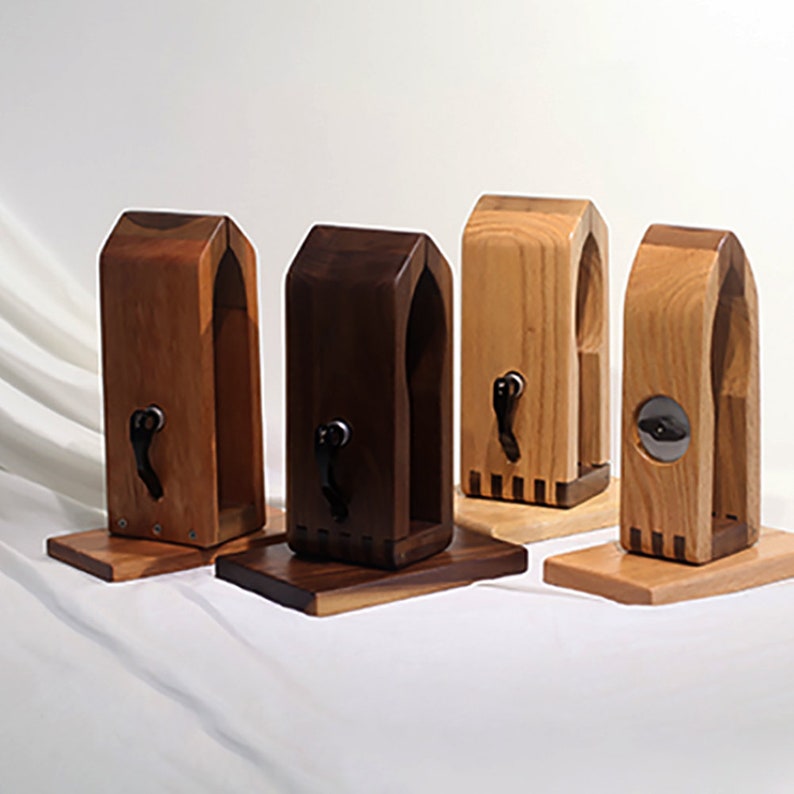 Puede incluir: Cuatro soportes para auriculares de madera en diferentes tonos de madera. Los soportes tienen un dise&ntilde;o de arco &uacute;nico y un peque&ntilde;o gancho de metal en la parte delantera. Los soportes se muestran sobre una superficie blanca.