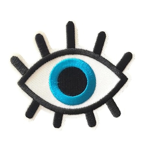 May include: A white embroidered eye patch with a black outline and a blue iris. The eye patch is a popular symbol of protection and good luck.