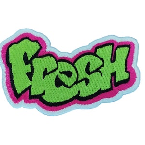 Puede incluir: Parche bordado verde con la palabra "fresh" en una fuente de estilo graffiti. Las letras están delineadas en negro y rosa.