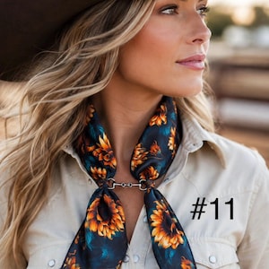May include: A dark-colored scarf featuring a vibrant sunflower pattern in shades of orange and yellow, secured at the neck with a silver-toned metal bit-style clasp. The scarf is worn over a light beige button-down shirt. The text #11 is visible.