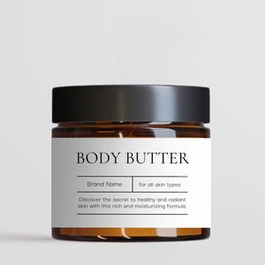 Peut inclure: Un pot en verre brun avec un couvercle noir et une étiquette blanche sur laquelle est inscrit "BODY BUTTER". L'étiquette comprend également le texte "Brand Name" et "for all skin types". Le texte "Discover the secret to healthy and radiant skin with this rich and moisturizing formula." est également présent sur l'étiquette.