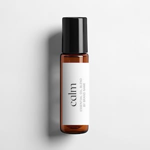 Puede incluir: Un frasco de vidrio marrón con tapa negra y una etiqueta blanca que dice "calm essential oil blend by brand name".