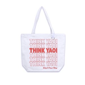 Puede incluir: Un bolso de tela blanco con dos asas. La parte frontal presenta el texto "THINK YAOI" repetido seis veces en rojo, con la línea central en rojo negrita. Debajo del texto, la frase "Ship It Your Way" está impresa en letras rojas pequeñas.