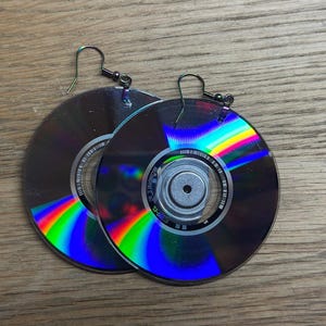 May include: A pair of earrings made from repurposed CDs. The earrings are silver with iridescent rainbow colors. The earrings are hanging from silver hooks.