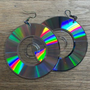 May include: A pair of iridescent rainbow earrings made from recycled compact discs. The earrings are circular and have a silver hook.