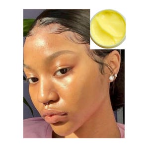 May include: A close-up of a person's face with a nose ring. The person has a light complexion and is wearing a purple shirt. A small jar of yellow cream is shown in the upper right corner of the image.