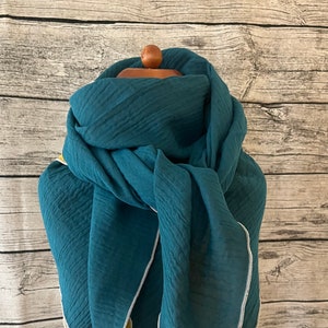 Può includere: Una sciarpa di cotone blu turchese con un bordo giallo e bianco. La sciarpa è piegata e drappeggiata su un manichino bianco.