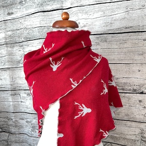 Może przedstawiać: Czerwony wełniany szalik z białym wzorem jelenia. Szalik ma strzępiony brzeg i jest prezentowany na białym manekinie.