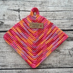 May include: A crocheted pot holder in pink, orange and purple with a brown tag that says "Handmade with Love".