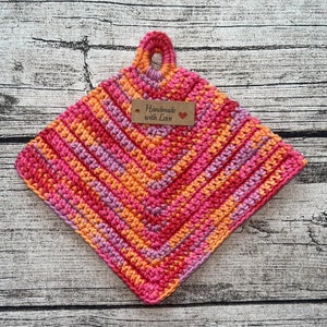Op de afbeelding: Een gehaakte pannenlappen in roze, oranje en paars met een bruin label waarop "Handmade with Love" en een klein rood hartje staat.