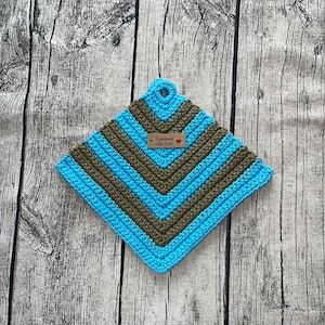 Op de afbeelding: Een handgemaakte gehaakte pannenlap in een vierkante vorm. De pannenlap heeft afwisselende strepen in turquoise en bruin. Een klein label met de tekst "Handmade with Love" is bevestigd. De pannenlap heeft een lus om op te hangen.