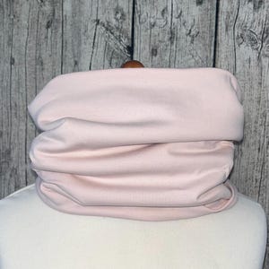 Op de afbeelding: Een zachte, roze stoffen nekwarmer of sjaal. De stof is gevouwen en geplooid om een ​​gezellige, warme look te creëren.