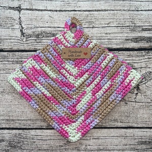 Może przedstawiać: Różowa, brązowa i biała dziana podkładka pod gorące z brązową metką z napisem "Handmade with Love".