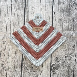 Op de afbeelding: Een handgemaakte gehaakte pannenlap in vierkante vorm met een ophanglus. De pannenlap heeft een chevronpatroon in lichtgrijze en roestkleurige strepen. Een klein label leest "Handmade with Love".